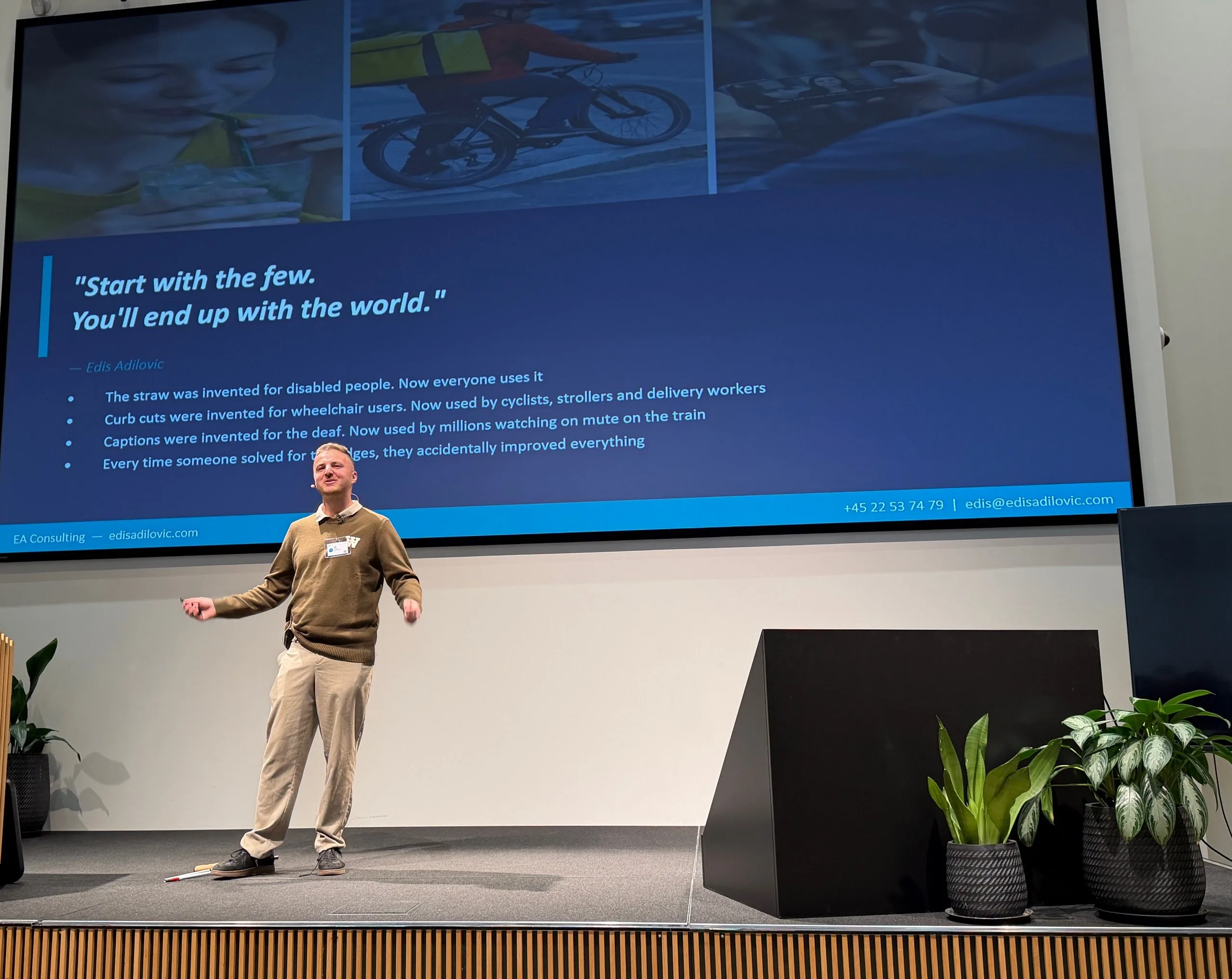 Edis holder foredrag om AI på en scene hos Microsoft. Han smiler og har armene ude til siden. Bag ham står hans eget citat på det store lærred, på engelsk: Start med de få, så ender du med hele verden.