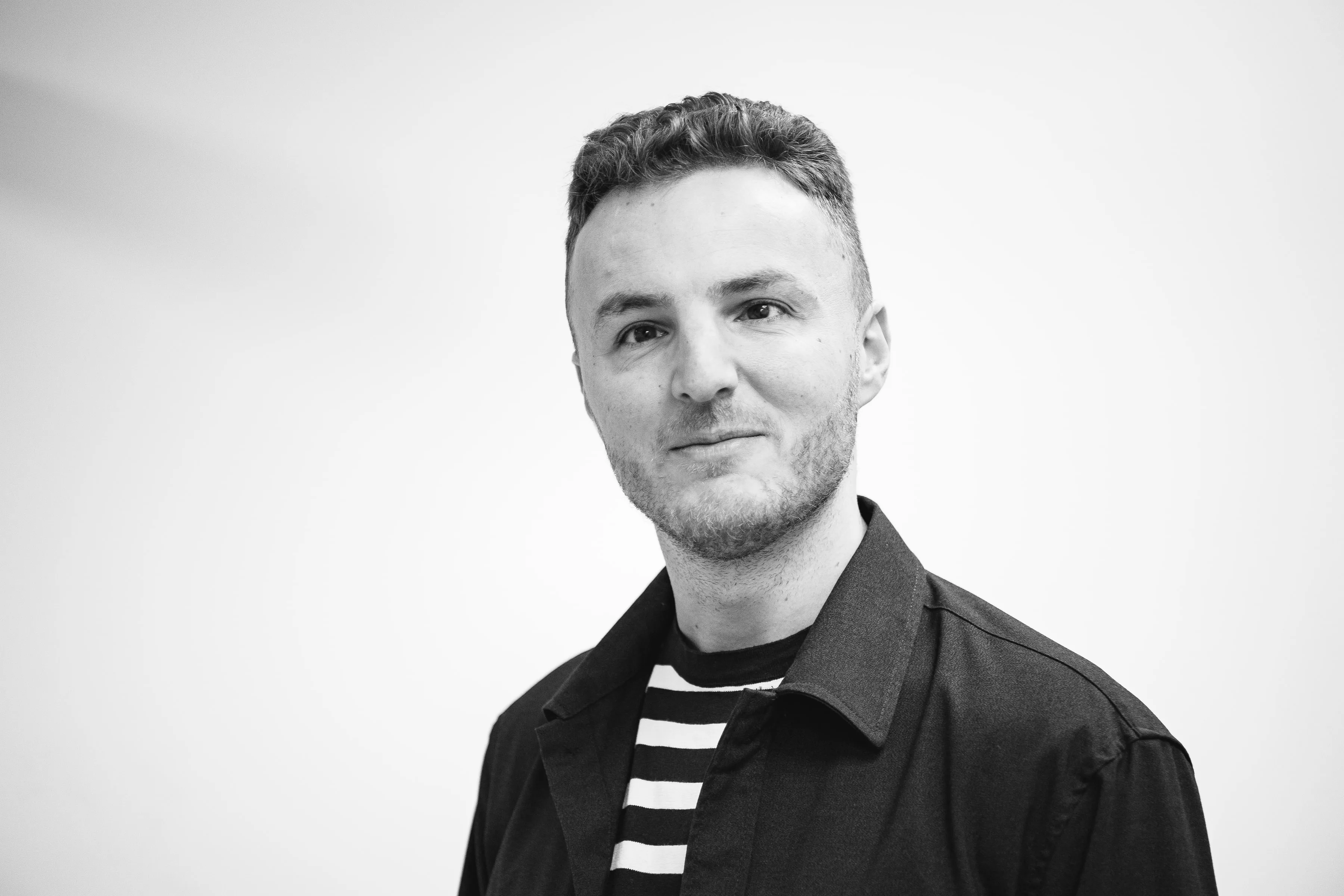 Black and white portrait of Edis smiling slightly at the camera.