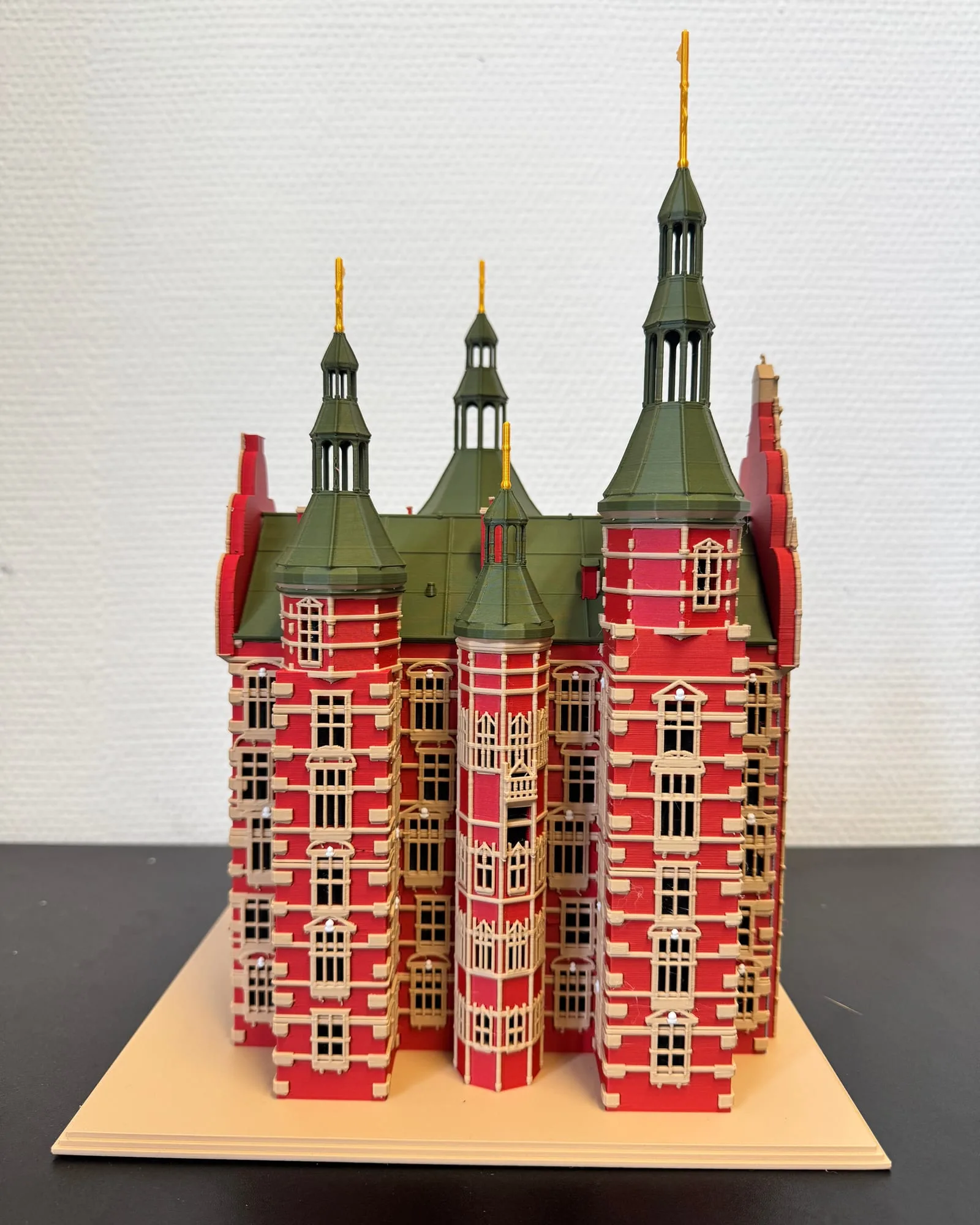 3D-printed model of Rosenborg Castle seen from the front on a sand-coloured base: four towers with green spires and golden vanes, red facades with raised sand-coloured window frames.