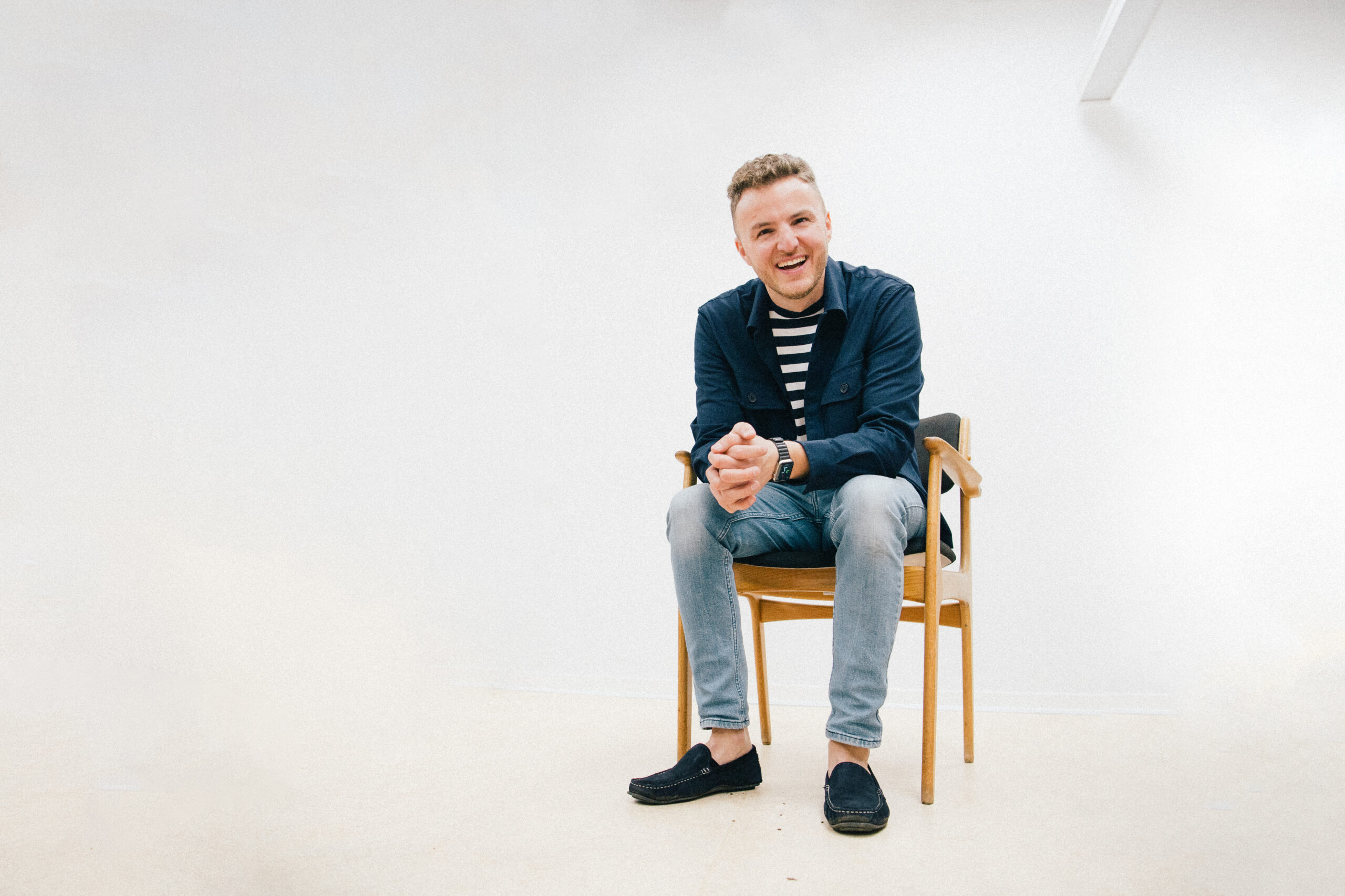 Edis sidder på en stol i lyst rum iført stribet trøje, mørk jakke og lyse jeans.