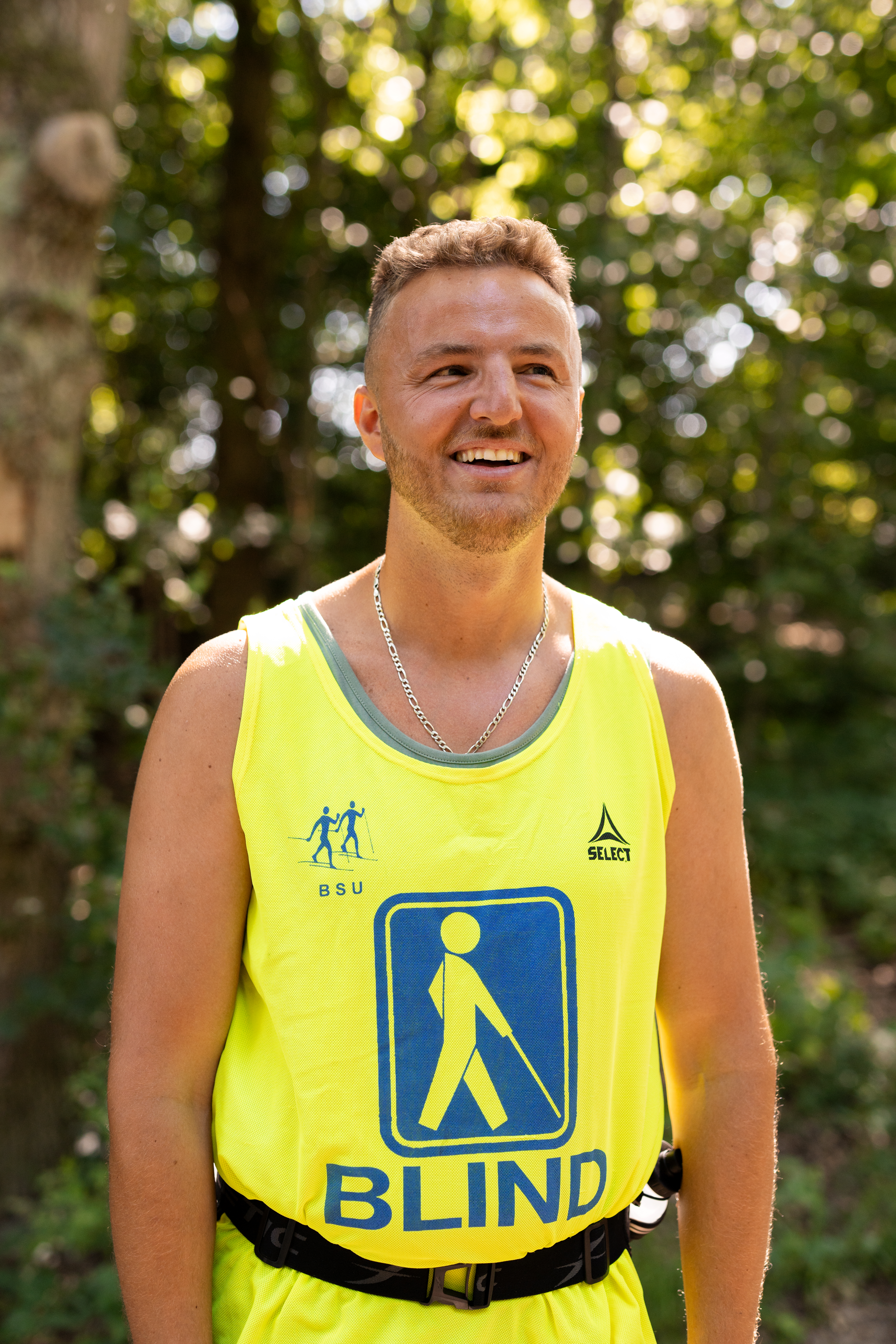 Edis smiler udendørs iført gul vest med blindesymbol og sølvkæde.